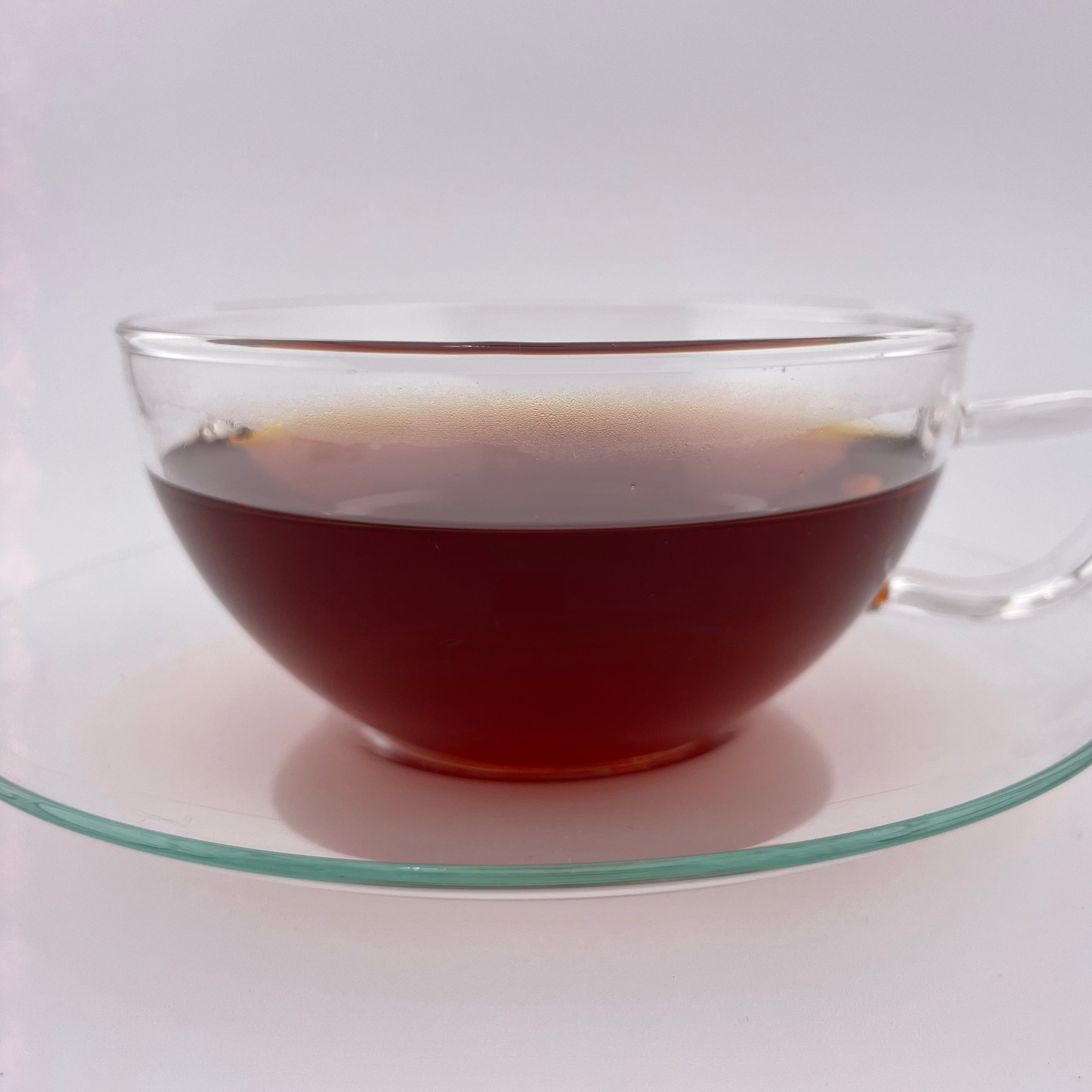 Clear glass mug filled with dark liquid on a matching glass saucer against a white background