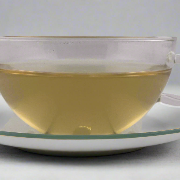 Clear glass teacup with tea on a matching saucer against a plain background