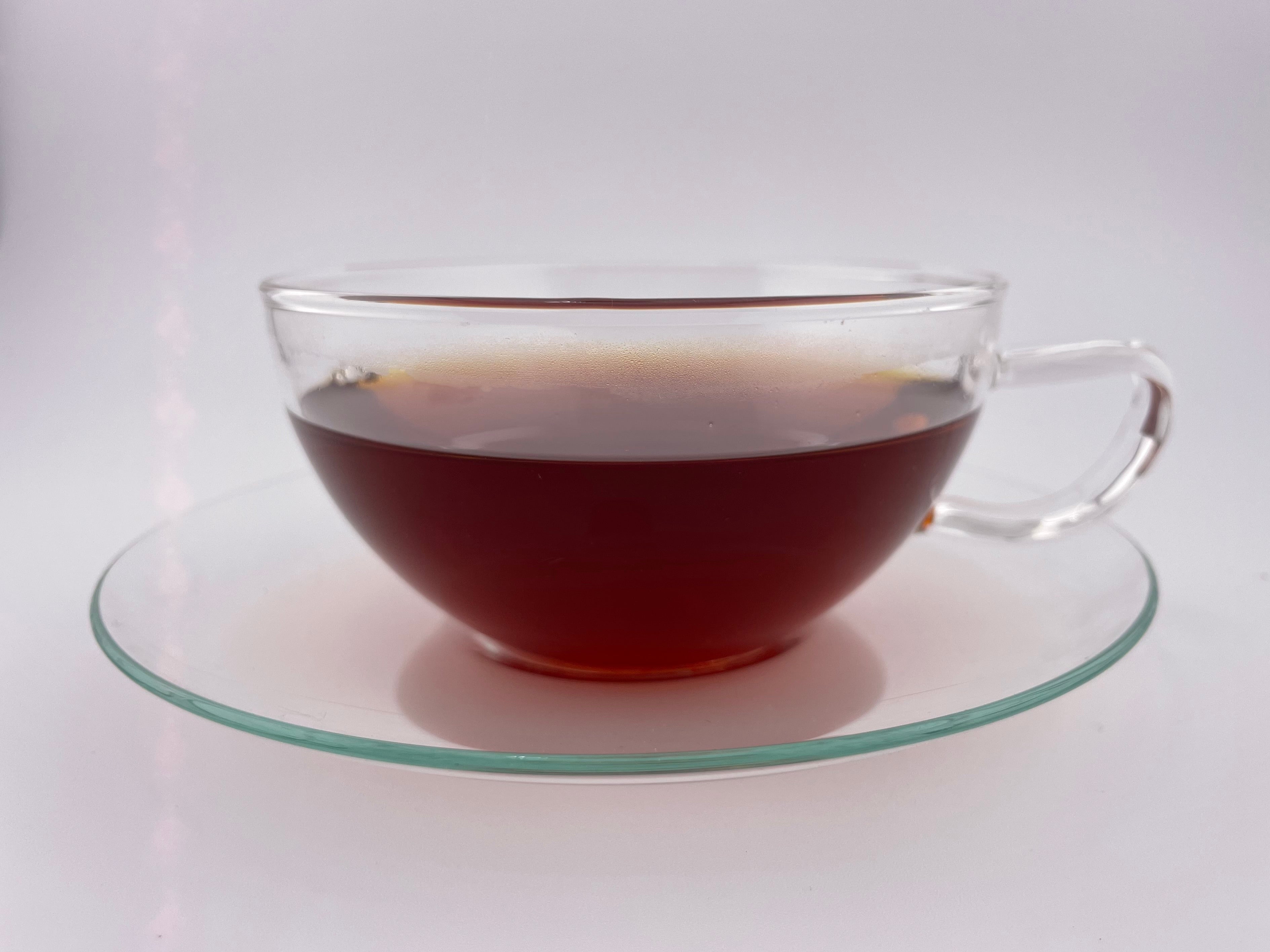 Clear glass mug filled with dark liquid on a matching glass saucer against a white background